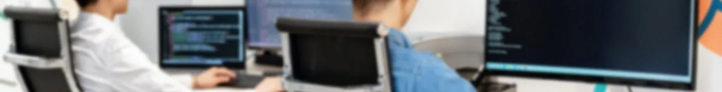 Duas pessoas trabalhando em estações com múltiplos monitores exibindo código